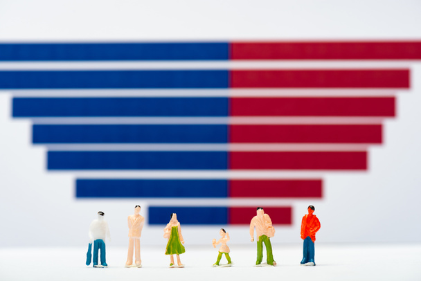 Селективный фокус пластиковых людей фигуры на белой поверхности вблизи синего и красного графиков на заднем плане, понятие равенства
 - Фото, изображение
