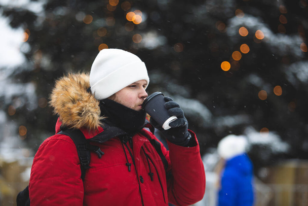 άνθρωπος σε εξωτερικούς χώρους πίνοντας καφέ από το φλιτζάνι χαρτί το χειμώνα ζεσταθεί κόκκινο παλτό - Φωτογραφία, εικόνα