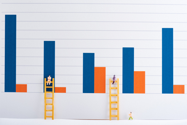 People figures with ladders on white surface with charts at background, equality concept - Фото, изображение