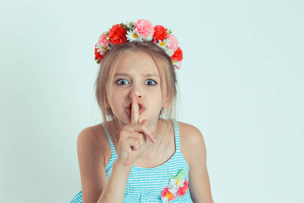 Portrait of beautiful woman with finger on lips, gesturing hush, keep silence, it is a secret. Closeup of Caucasian kid model with floral headband isolated on white green gray copy space background - Photo, Image