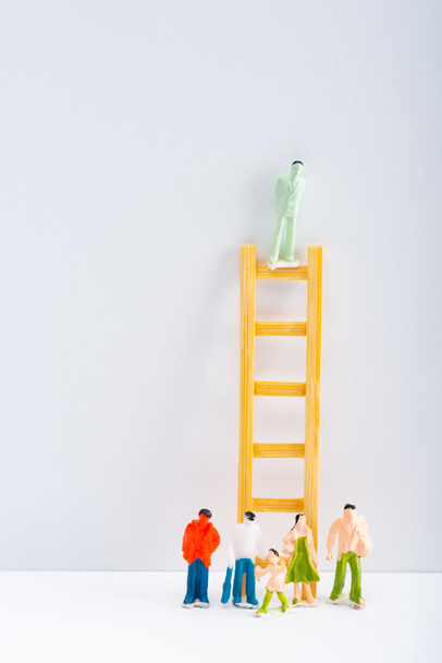 Doll on ladder with people figures on white surface on grey background, concept of equality rights  - Photo, Image