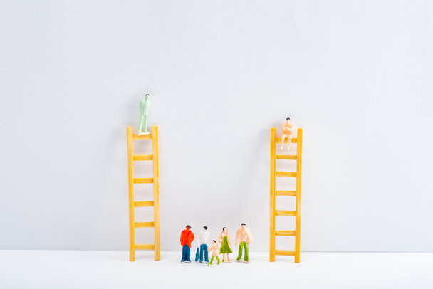 Dolls on ladders with people figures on white surface on grey background, concept of equality rights  - Photo, Image