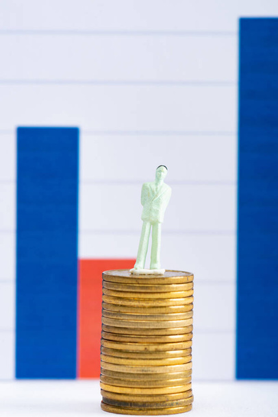 Koncepce finanční rovnosti s lidmi figurka na skládaných mincí na bílém povrchu s grafy na pozadí - Fotografie, Obrázek