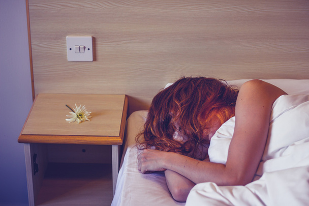 Woman sleeping in hotel room with flower next to her face - Foto, Bild