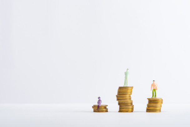 Três pessoas figuras em moedas empilhadas na superfície branca isolado em cinza, conceito de igualdade financeira
 - Foto, Imagem