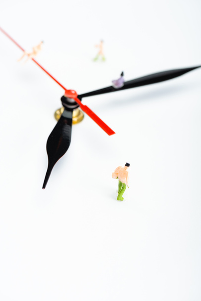 Vista de ángulo alto de las flechas del reloj y figuras de personas de plástico en la superficie blanca, concepto de senescencia
 - Foto, Imagen