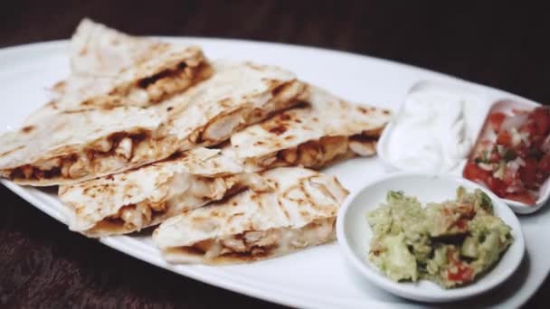 Sliced chicken and cheese quesadilla served with guacamole, pico de gallo and sour cream dip - video in slow motion - Footage, Video