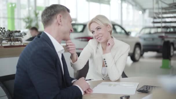 Portrait of young woman flirting with car dealer in showroom. Confident Caucasian businesswoman in elegant white suit touching traders face and smiling. Flirt, seduce, lifestyle, wealth. - Imágenes, Vídeo