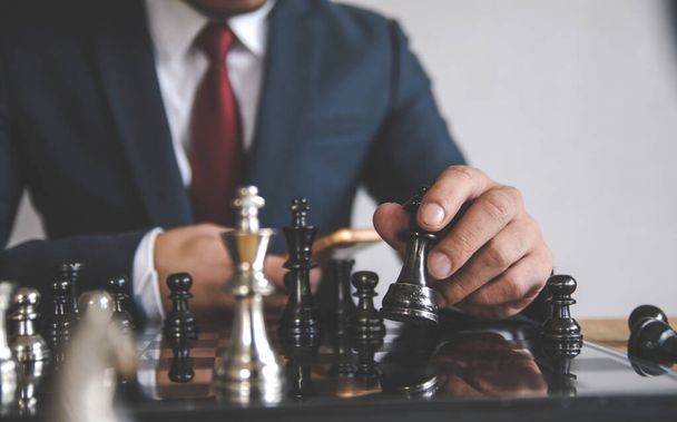 Retro style image of a businessman with clasped hands planning strategy with chess figures on an old wooden table. - Foto, Imagem