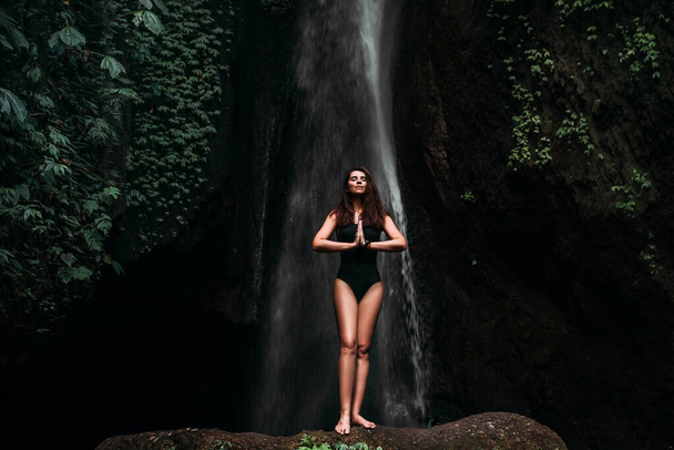 A woman does yoga at a waterfall. Healthy lifestyle. The concentration of the body. A woman does yoga in Bali. A woman meditates in nature. Meditation at the waterfall. Young woman practicing yoga - Foto, immagini
