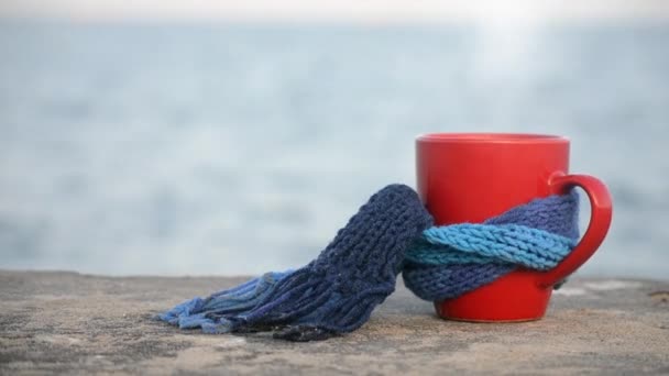 Red mug with coffee and steam tied with blue knitted scarf stands on stone - Footage, Video