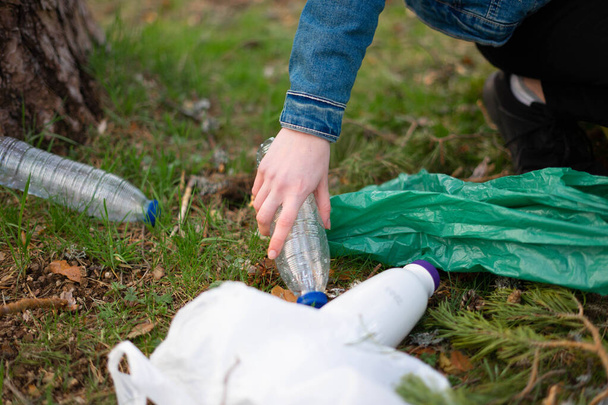 Στενή άποψη ενός έφηβου κοριτσιού χέρι συλλογή πλαστικών στο δάσος. Έννοια βιωσιμότητας. - Φωτογραφία, εικόνα