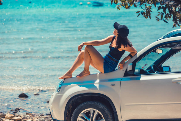 γυναίκα κάθεται στο αυτοκίνητο κουκούλα κοιτάζοντας στη θάλασσα παραλία παραθαλάσσιες καλοκαιρινές διακοπές - Φωτογραφία, εικόνα