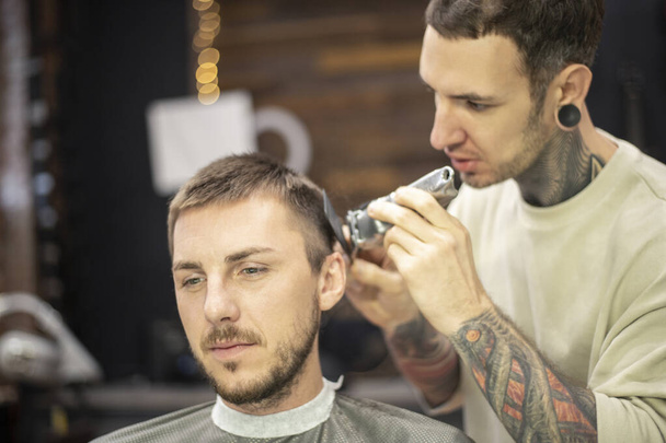 Friseur benutzt Rasiermesser, während er männlichen Kunden beim Friseur eine Frisur schneidet - Foto, Bild