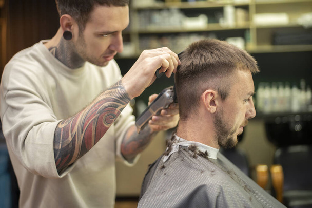 Fryzjer za pomocą golarki elektrycznej, zapewniając fryzurę dla klienta płci męskiej w zakładzie fryzjerskim - Zdjęcie, obraz
