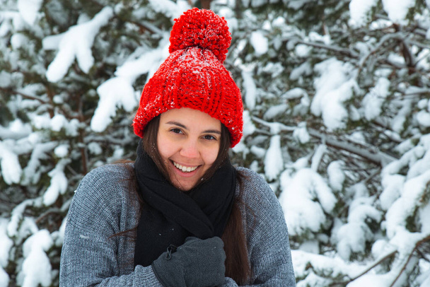 portrait of young smiling woman in winter clothes in red hat with bubo fir tree in background. stylish concept - Photo, Image