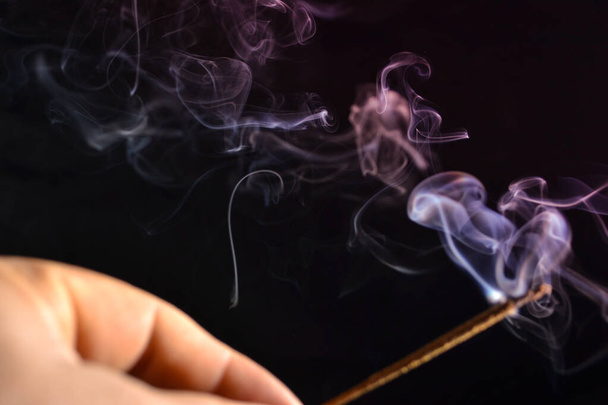 Hand holds a stick of incense game of smoke on a dark background - Fotoğraf, Görsel