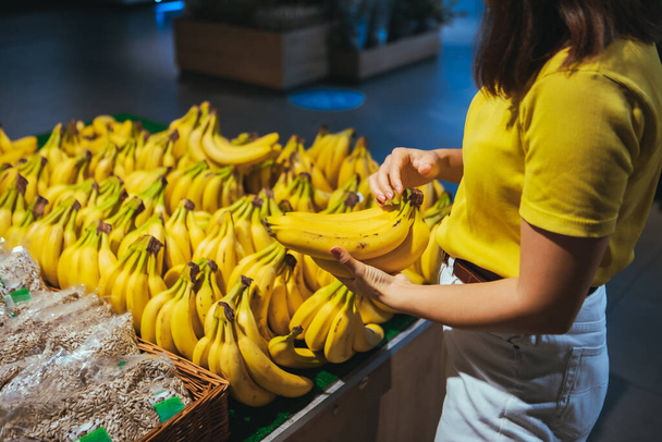 vrouw het nemen van gele bananen uit de winkel plank kruidenier winkelen concept - Foto, afbeelding