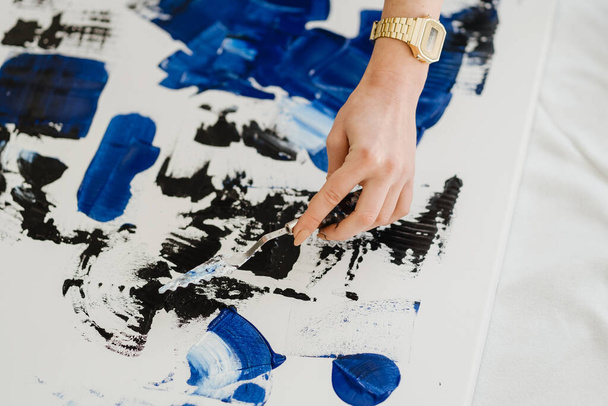 Blisko kobiet ręka rysunek na białym płótnie za pomocą widmo niebieski i czarny farba olejna - Zdjęcie, obraz