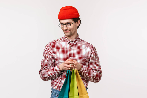 Waist-up portrait mysterious and funny cute boyfriend looking cunning camera and smirk sly as holding shopping bags, have perfect idea what buy for girlfriend, go to store together, white background - Foto, immagini