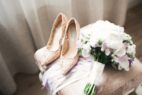 Brides wedding shoes with a bouquet with roses and other flowers on tha arm chair - Fotó, kép