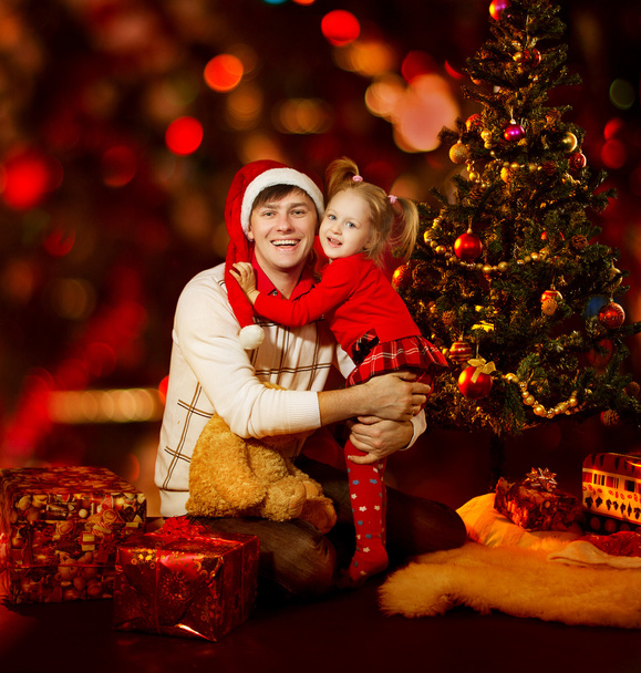 Jouluperhe. Isä ja tytär Kid joulukuusen alla, punainen
 - Valokuva, kuva