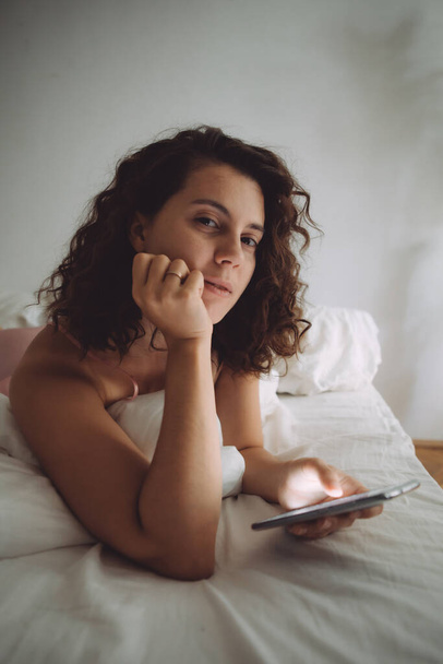 young pretty woman with curly hair in bed with phone domestic lifestyle - Foto, Imagen