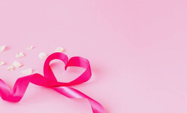 Juhlava vaaleanpunainen nauha sydämen muodossa vaaleanpunaisella taustalla valkoisilla ruusun terälehdillä. Malli mallina onnittelukortin tai tekstin suunnittelu. Lähikuva, kopioi tilaa
 - Valokuva, kuva