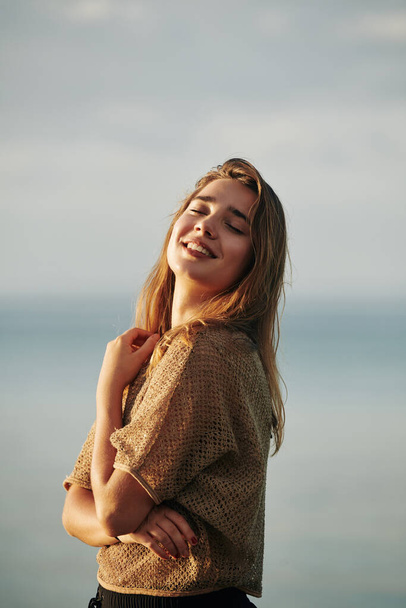 Portrait of young beautiful woman enjoying sea breeze and sunset sun rays - Foto, Imagem
