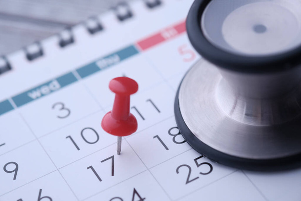 Regular medical examination concept, black stethoscope and push pin on calendar background - Zdjęcie, obraz