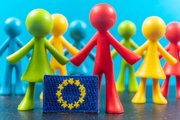 Crowd of multicolored plastic human figures with Flag of Europe or European Flag. Concept of believe in a united Europe. Selective focus - Photo, Image