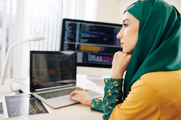 Όμορφη σκεπτική νεαρή γυναίκα με παραδοσιακή χιτζάμπ εργάζεται στον προγραμματισμό κώδικα για τους μαθητές του έργου - Φωτογραφία, εικόνα