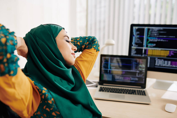 Mujer musulmana joven estirándose en su silla después de trabajar en el código de programación
 - Foto, Imagen