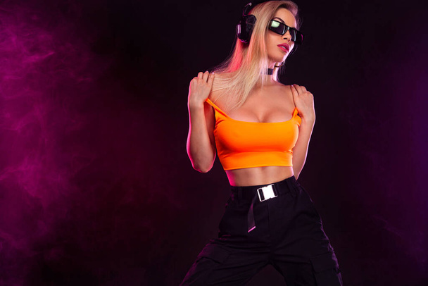 Sporty fit woman dancer and dj with headphones in sunglasses on dark background. - Foto, immagini