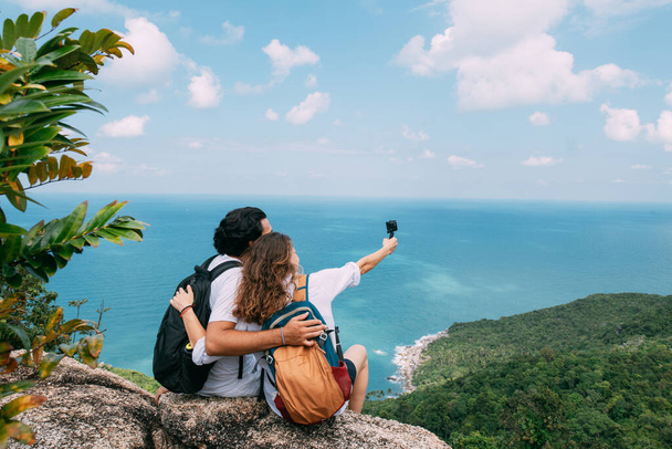 A couple stand on a rock at a viewpoint with an epic view of the ocean. A popular tourist destination. Lovers on vacation in the tropics. Honeymoon in the tropics. - Фото, изображение