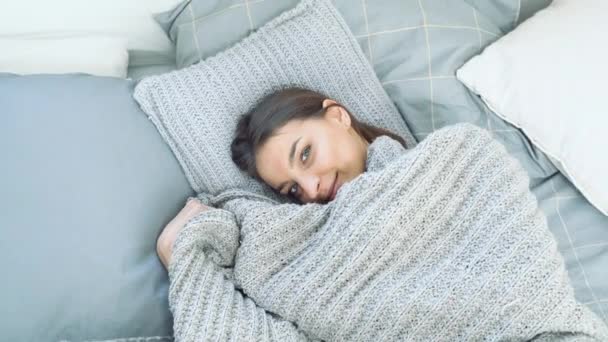 Портрет молодой красивой женщины, выглядывающей из-под одеяла и наслаждающейся утром в постели дома
. - Кадры, видео