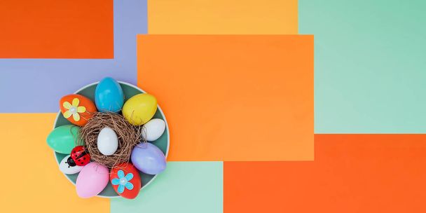 Fényes háttér aszimmetrikus geometriai mintával trendi színekben, húsvéti tojásaik összetételével, katicabogárral és tányéron fekvő virágokkal. Koncepció háttér, ünnep, húsvét - Fotó, kép