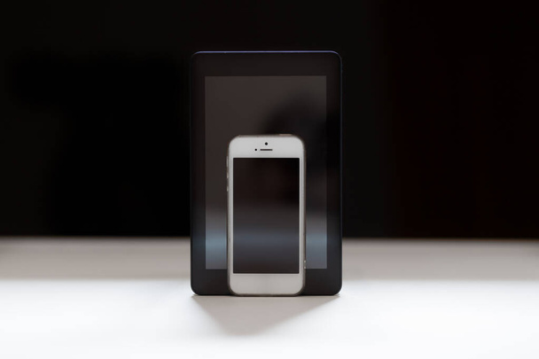 Tablet und Handy auf schwarzem Hintergrund mit schwarzen Bildschirmen. - Foto, Bild