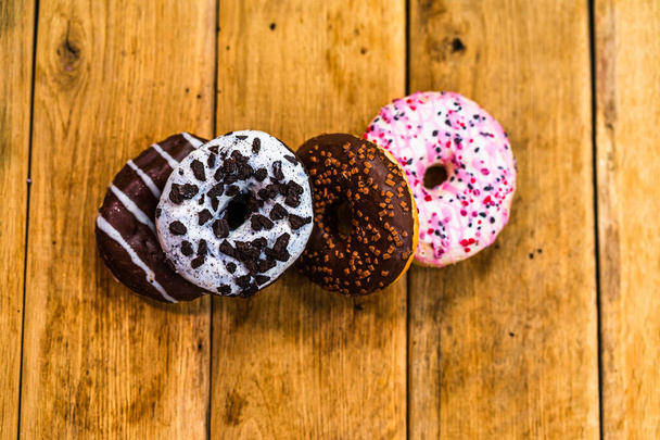 Bunte Donuts auf einem Holztisch. Süße Puderzucker-Nahrung mit glasierten Streusel, Donut mit Schokolade Zuckerguss. Draufsicht mit Kopierraum - Foto, Bild