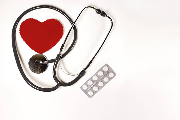 Egészségügyi Világnap, egészségügy és orvosi koncepció. Piros szív sztetoszkóppal és fehér pirulák fehér háttér textúra - Fotó, kép