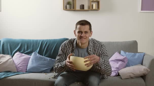 Worried young man watching tv and throwing popcorn to camera - Materiał filmowy, wideo