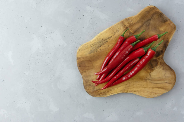 Φρέσκες κόκκινες καυτερές πιπεριές τσίλι βρίσκονται σε μια ξύλινη σανίδα σε γκρι φόντο. Μεξικάνικο καρύκευμα. Θέση για το κείμενο σας - Φωτογραφία, εικόνα
