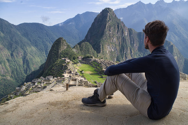 Biały młodzieniec siedzący i oglądający niesamowity krajobraz Machu Picchu. Peru, Ameryka Południowa - Zdjęcie, obraz