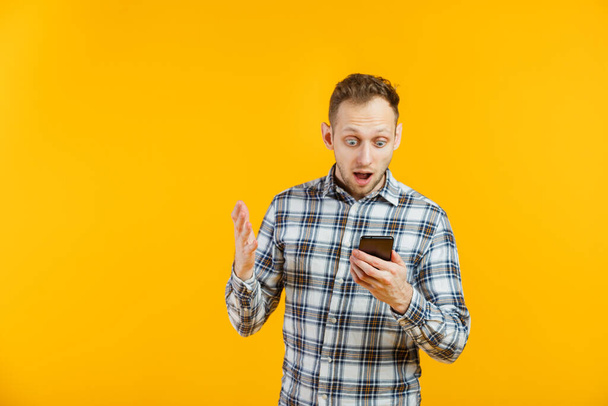 Retrato de chocado estudante do sexo masculino isolado em amarelo com seu smartphone na mão
 - Foto, Imagem