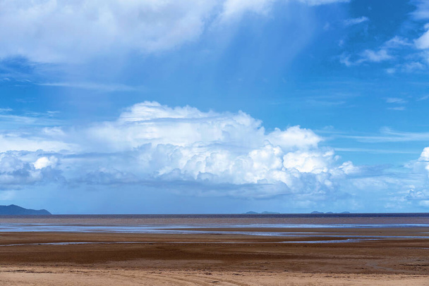 Witte pluizige wolken in een heldere blauwe lucht boven een getijdenstrand met het water teruggetrokken - Foto, afbeelding