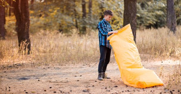 Autumn lifestyle of man inflates an inflatable orange sofa in forest. Relaxing and enjoying life on air bed banner format - 写真・画像