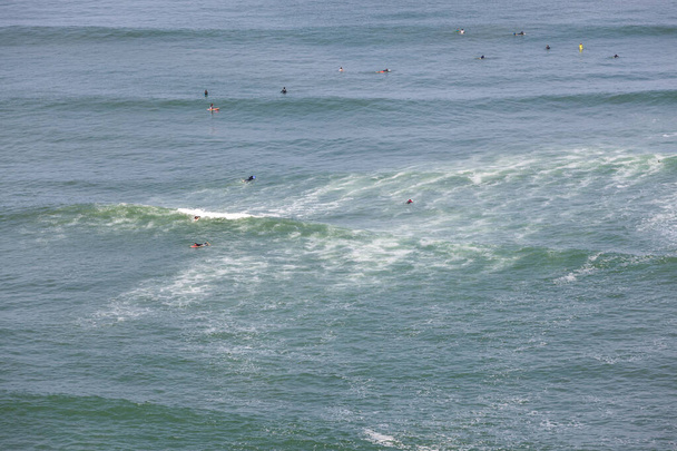 Uma multidão de pessoas não identificáveis desfrutando das ondas enquanto surfam em trajes úmidos completos nas águas frias do Pacífico Sul-Americano em Lia, Peru
. - Foto, Imagem