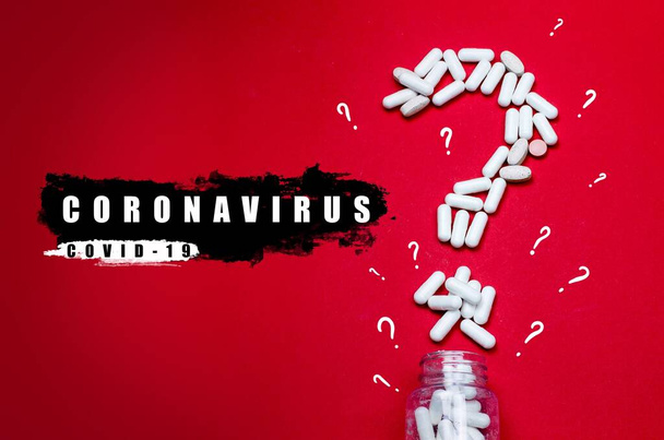 Stetoskop ze słowami CORONA VIRUS 2019 COV na czerwonym tle. Selektywne skupienie i fragment ziarna ze znakiem zapytania zrobionym z białych tabletek - Zdjęcie, obraz