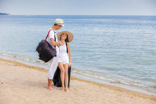 Νεαρό ζευγάρι ερωτευμένο στην παραλία με ταξιδιωτικές τσάντες - Φωτογραφία, εικόνα