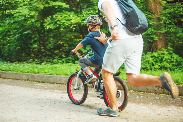 father teaching son how to ride bicycle. summer time. public park - Fotografie, Obrázek